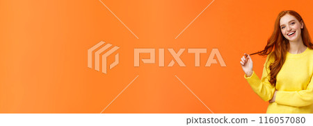 Carefree good-looking, smiling toothy redhead woman, girl with ginger hair laughing as chatting friends, rolling curl on hair, tilt head and smiling joyfully, having conversation, orange background 116057080