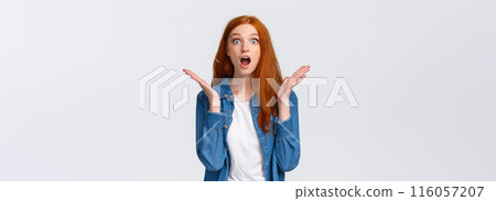 Surprised speechless redhead female learn excellent news, cant believe dream come true, staring camera drop jaw, gasping and raise hands sideways amazed, white background 116057207