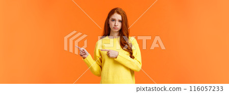 Sulking moody and sad cute redhead girlfriend pointing right and frowning, standing unhappy with bad mood, envy someone, begging boyfriend book tickets for winter ski-resort, orange background Sulking moody and sad cute redhead girlfriend pointing right and frowning, standing unhappy with bad mood, envy someone, begging boyfriend book tickets for winter ski-resort, orange background 116057233