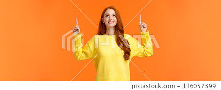 Dreamy happy and upbeat redhead young modern woman gazing up with satisfied smile. Gorgeous girl ginger hair conemplate top advertisement, pointing upwards, standing orange background 116057399