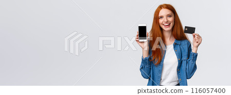 Shopping, application and mobile concept. Waist-up portrait friendly charismatic female blogger, redhead girl promote bank service, showing smartphone or app on display and credit card, smiling 116057400