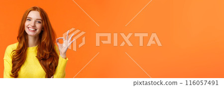 Satisfied consumer recommends product. Cute cheerful feminine redhead woman with pretty smile, showing okay gesture, like, agree or approve something, giving positive feedback, orange background 116057491