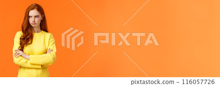 Offended angry and tensed woman with curly red hair, freckles, having bad mood, cross arms chest, thinking troublesome situation, frowning getting mad, standing orange background distressed 116057726