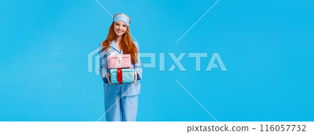 Cheerful and lovely young happy redhead woman waking up early christmas eve congratulating with winter holidays, wearing pyjama and sleep mask, holding boxes with gifts, giving presents 116057732