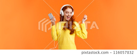 Technology, emotions and gadgets concept. Cheerful good-looking redhead woman dancing with hands up, closed eyes, smiling joyfully, enjoy awesome music sound in headphones, hold smartphone 116057832