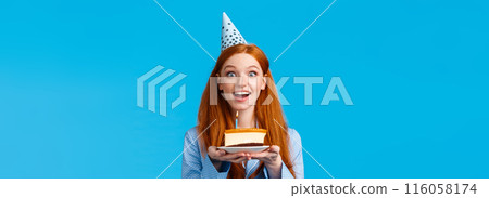 Waist-up portrait cheerful and upbeat cute smiling redhead feminine girl i b-day cap, holding piece birthday cake, excited celebrating own birthday, standing sleepwear over blue background 116058174