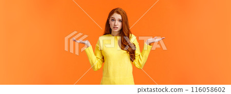 Perplexed cute redhead girl, shrugging with raised arms and looking confused, dont know answer, cant help, feeling confused or indecisive, cannot understand, standing orange background 116058602