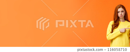 Sulking moody and sad cute redhead girlfriend pointing right and frowning, standing unhappy with bad mood, envy someone, begging boyfriend book tickets for winter ski-resort, orange background 116058710