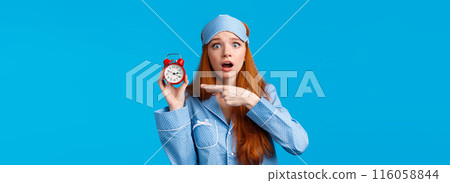 Shocked and concerned, worried cute redhead girl pointing at alarm clock with frustrated, nervous expression, being late, dont know how set up right time, standing blue background in nightwear Shocked and concerned, worried cute redhead girl pointing at alarm clock with frustrated, nervous expression, being late, dont know how set up right time, standing blue background in nightwear 116058844