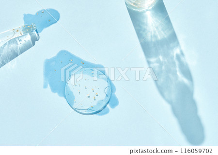 Serum gel texture swatch. Transparent drop golden sparkles. Blue background 116059702