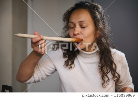 Close-up portrait of a woman trying pasta sauce to test the taste. Italian young pretty woman sampling food, enjoying the taste, standing with her eyes closed in the minimalist home kitchen interior Close-up portrait of a woman trying pasta sauce to test the taste. Italian young pretty woman sampling food, enjoying the taste, standing with her eyes closed in the minimalist home kitchen interior 116059969