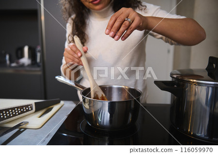 Pretty woman, housewife spilling salt while cooking tomato sauce. Female chef in the home kitchen, sprinkling salt while seasoning meal with a pinch of salt. People. Food and drink consumerism Pretty woman, housewife spilling salt while cooking tomato sauce. Female chef in the home kitchen, sprinkling salt while seasoning meal with a pinch of salt. People. Food and drink consumerism 116059970