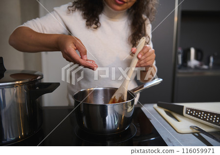 Close-up female chef's hands adding a pinch of salt to the tomato sauce, mixing stirring ingredients while preparing sauce for seasoning Italian pasta. Woman cooking spaghetti for family dinner Close-up female chef's hands adding a pinch of salt to the tomato sauce, mixing stirring ingredients while preparing sauce for seasoning Italian pasta. Woman cooking spaghetti for family dinner 116059971