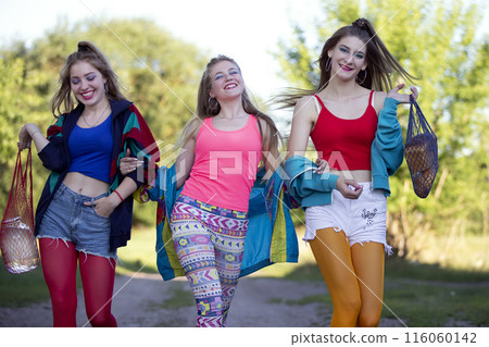 Three beautiful country girls dressed in the style of the nineties are walking along the road. 116060142