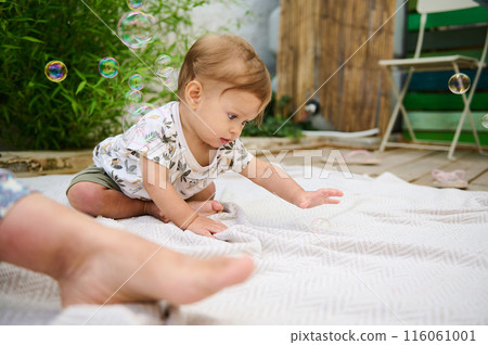 Cute baby boy playing with soap bubbles in the patio backyard. Redhead Caucasian child catches bubbles outdoors, showing interest to flying bubbles. Children, Childhood. Education and learning Cute baby boy playing with soap bubbles in the patio backyard. Redhead Caucasian child catches bubbles outdoors, showing interest to flying bubbles. Children, Childhood. Education and learning 116061001