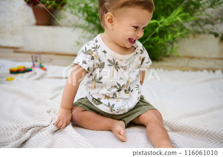 Authentic portrait of redhead Caucasian toddler, cheerful smiling baby boy sitting on beige blanket outdoors. Happy carefree childhood, infancy and babyhood concept Authentic portrait of redhead Caucasian toddler, cheerful smiling baby boy sitting on beige blanket outdoors. Happy carefree childhood, infancy and babyhood concept 116061010