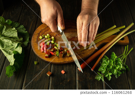 The cook is preparing a vitamin salad on the kitchen table. Close-up of a chef's hands cutting fresh rhubarb stalks with a knife. Place for advertising 116061268