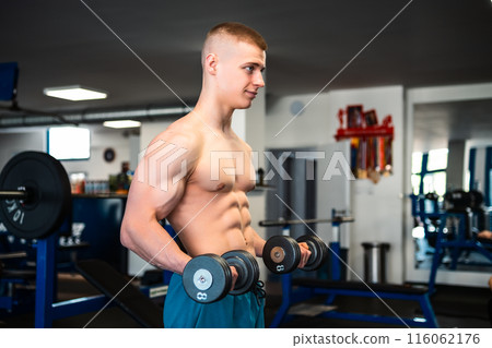 A young man lifting weights in a gym. Professional bodybuilder training in the gym 116062176