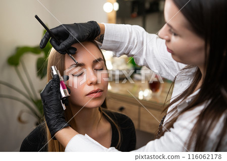 Beauty master styling clients eyebrows in a salon.  116062178