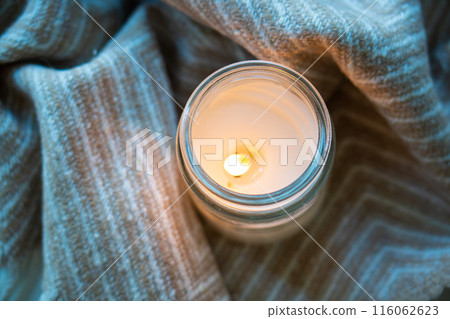 The image shows a top view of a lit candle with a blanket, creating a cozy and warm atmosphere The image shows a top view of a lit candle with a blanket, creating a cozy and warm atmosphere 116062623