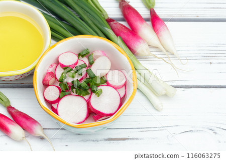 Salad of sliced radishes (French breakfast variety) and green onions in a little bowl, all ingredients with olive oil are on the white wooden rustic table. 116063275