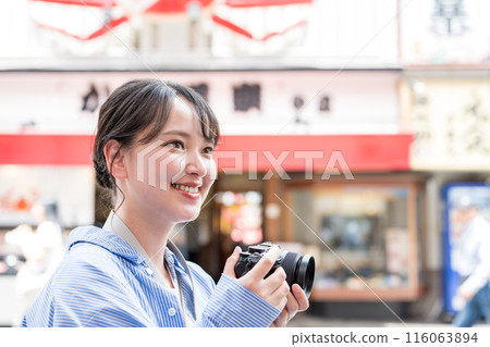 Image of a young and pretty woman enjoying her hobby of photography in a busy street | Image of a female photographer 116063894