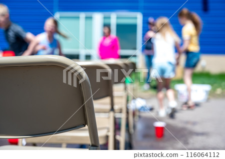 Selective focus on the back of a metal folding chair with blurred children playing end of school games. 116064112