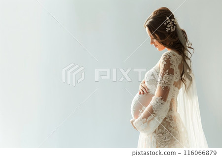 A pregnant woman stands in front of a white background wearing a white gown 116066879