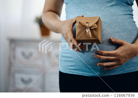 Close-up of pregnant woman in blue tank top holding small gift box with brown ribbon Close-up of pregnant woman in blue tank top holding small gift box with brown ribbon 116067936