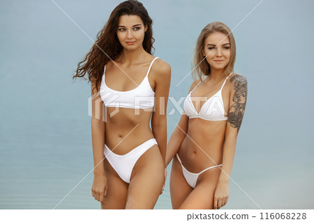 Happy Women in White Bikinis Holding Hands on Beach Walk 116068228