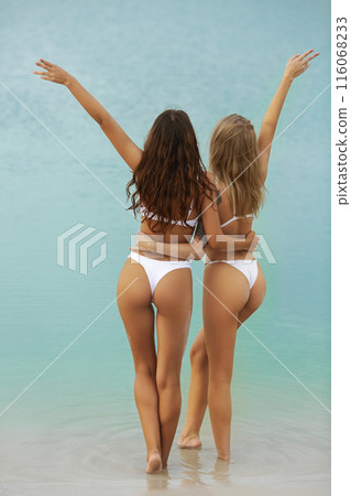 Two Slim, Tanned Women in White Bikinis Celebrating Freedom by the Sea 116068233