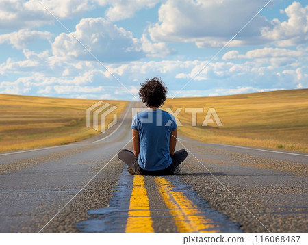 A person sits cross-legged on a deserted road, gazing at the endless horizon under a sky filled with fluffy clouds. 116068487