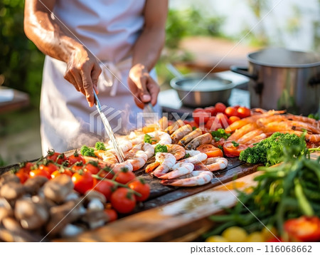 A chef grills shrimp, tomatoes, and other vegetables on an outdoor grill, surrounded by fresh ingredients. 116068662