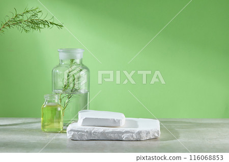 The photo was taken from front angle over green background. An empty white podium displayed on gray lab table top, next to a glass bottle of transparent liquid and another contains yellow liquid 116068853