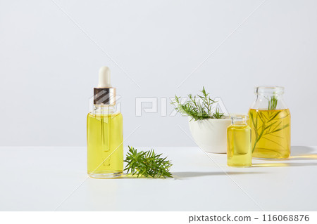An unbranded serum bottle with yellow essential oil placed on white counter top, on the other side displaying two glass bottles of yellow liquid and a white ceramic bowl. Front view, designing space An unbranded serum bottle with yellow essential oil placed on white counter top, on the other side displaying two glass bottles of yellow liquid and a white ceramic bowl. Front view, designing space 116068876