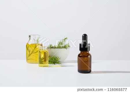 White background photo with a blank label serum bottle in brown color standing out, decorated with some glassware of yellow essence and tea trees contained in ceramic bowl White background photo with a blank label serum bottle in brown color standing out, decorated with some glassware of yellow essence and tea trees contained in ceramic bowl 116068877