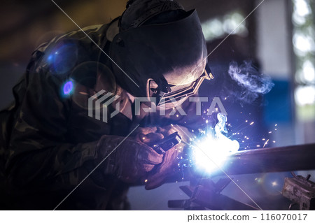 Welder at work. Man in a protective mask. The welder makes seams on the metal. Sparks and smoke when welding. 116070017
