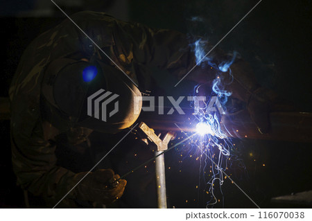 Welder at work. Man in a protective mask. The welder makes seams on the metal. Sparks and smoke when welding. 116070038
