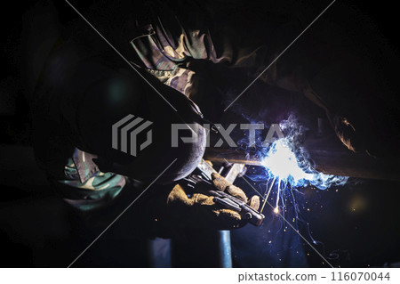Welder at work. Man in a protective mask. The welder makes seams on the metal. Sparks and smoke when welding. 116070044