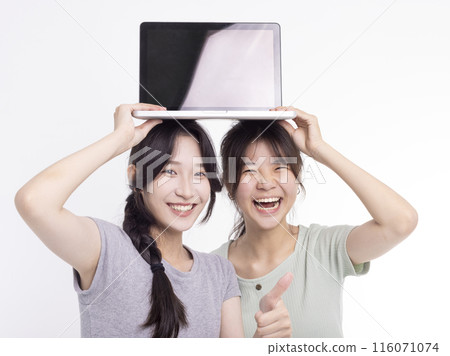 Two young beautiful smiling asian teenager female holding the laptop Two young beautiful smiling asian teenager female holding the laptop 116071074
