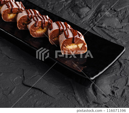 Chocolate drizzled profiteroles on dark plate Chocolate drizzled profiteroles on dark plate 116071396
