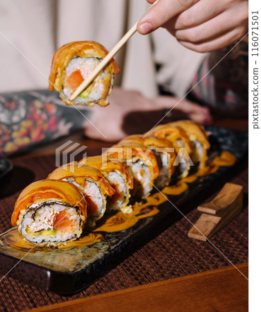 Person holding sushi roll with chopsticks Person holding sushi roll with chopsticks 116071501