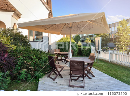 A patio with a large umbrella and several chairs. The chairs are arranged around a dining table 116073290