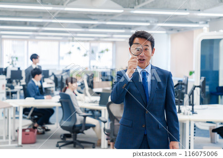 Middle-aged businessman using a magnifying glass in the office Middle-aged businessman using a magnifying glass in the office 116075006