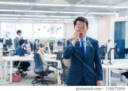Middle-aged businessman using a magnifying glass in the office 116075009
