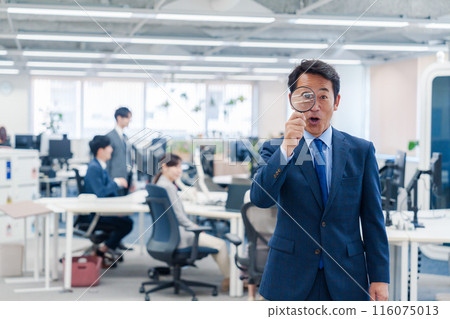 Middle-aged businessman using a magnifying glass in the office 116075013