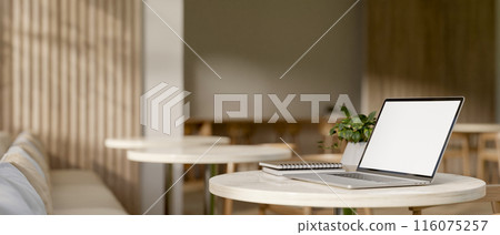 A laptop computer with a white-screen mockup on a table in a modern, comfortable coffee shop. A laptop computer with a white-screen mockup on a table in a modern, comfortable coffee shop. 116075257