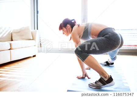 Beautiful redhead woman's home fitness routine. Home workout on gym mat in living room, sporty woman wearing sportswear. 116075347