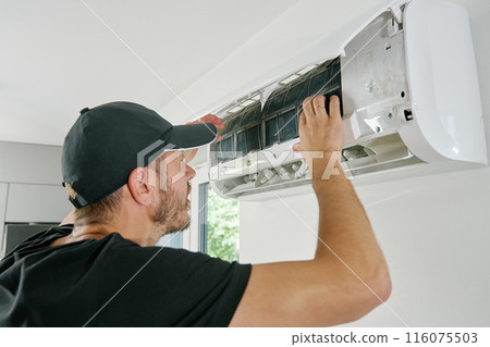 Air conditioner maintenance. Male technician repairs home climate system in living room. Man is cleaning filters of conditioner Air conditioner maintenance. Male technician repairs home climate system in living room. Man is cleaning filters of conditioner 116075503