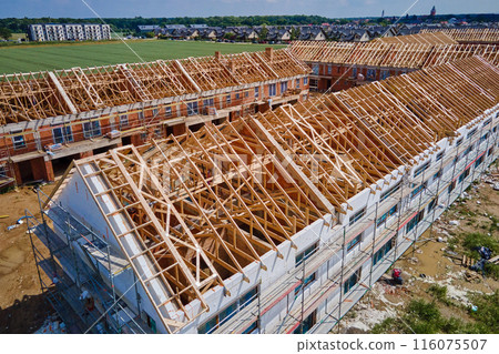 Aerial view of new house construction project in suburban area. Residential building wooden roof frame with truss, post and beams at construction site. Manufacture of new neighborhood in small town 116075507